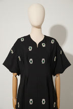 Black dress with green and silver embellishments on a mannequin against a gray background