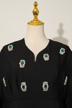 Black dress with green and white floral embellishments on a mannequin against a gray background