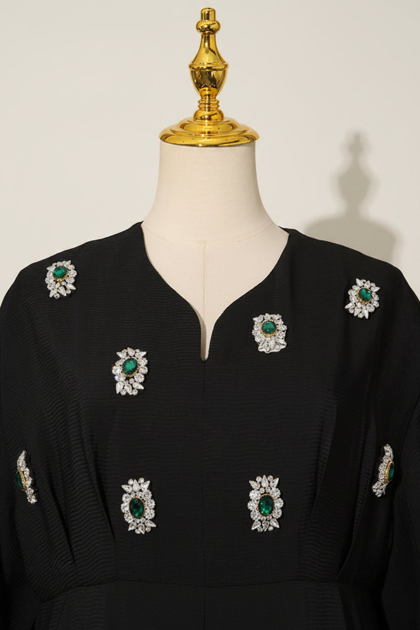 Black dress with green and white floral embellishments on a mannequin against a gray background
