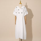 White dress with decorative elements on a mannequin against a gray curtain background