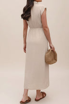 Woman in a beige dress holding a straw bag in a minimalistic room with wooden shelves.