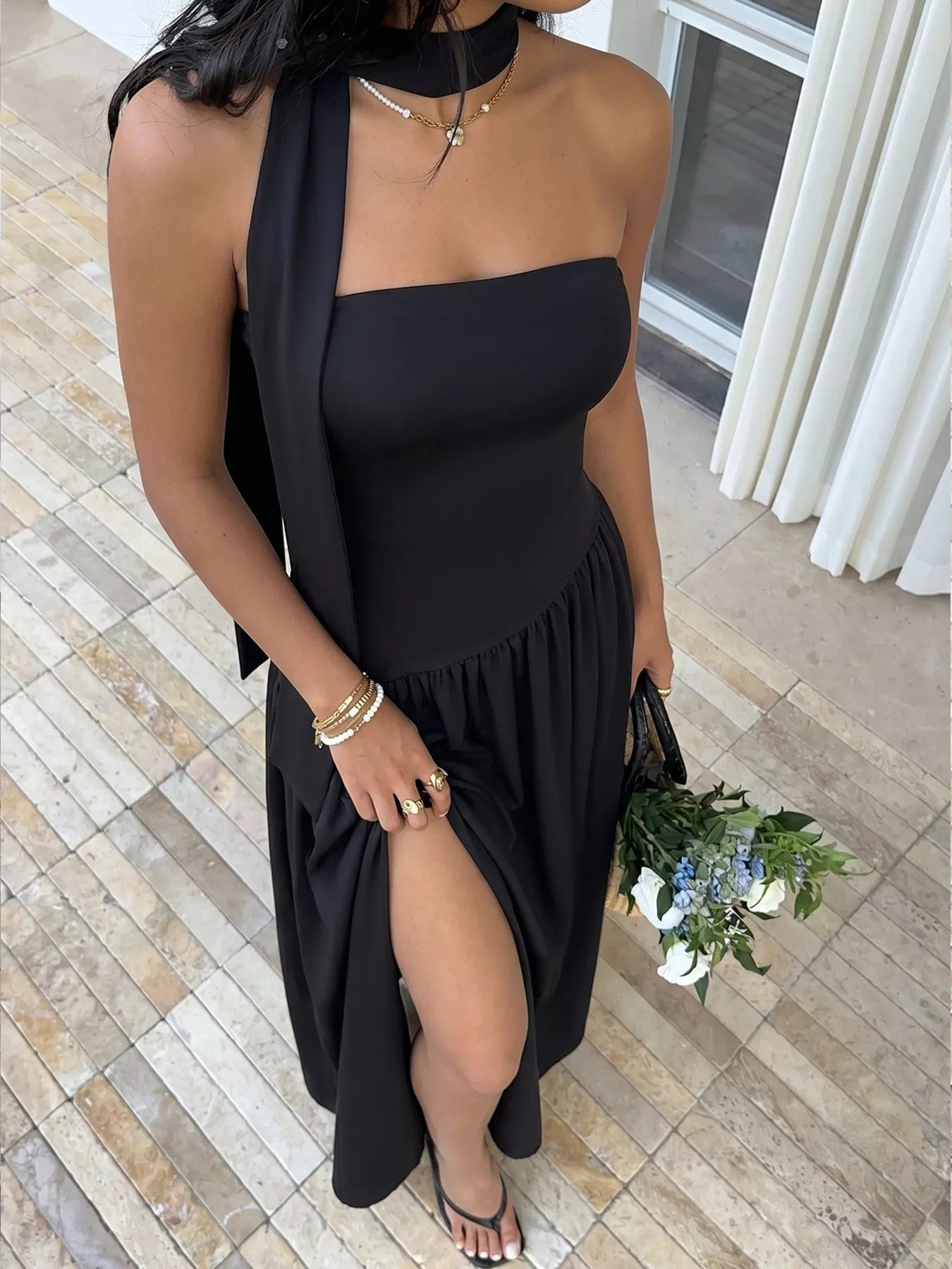 Woman in a black dress holding flowers on a tiled floor.