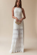 Woman in a white halter neck dress holding a gold clutch in a room with shelves.
