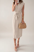 Woman wearing a beige dress holding a straw bag in a minimalistic room.