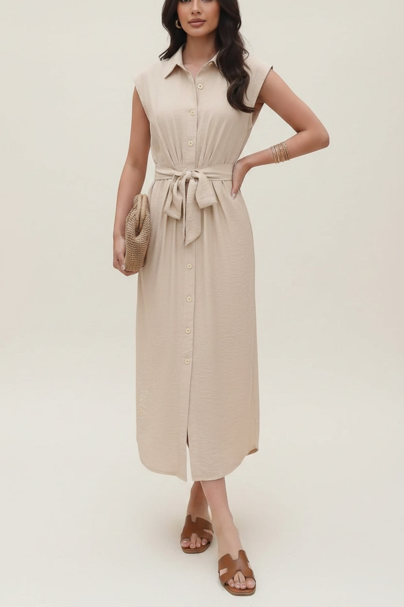 Woman wearing a beige dress standing in front of wooden shelves.