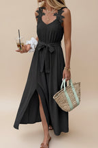 Woman wearing a black dress with lace details, holding a straw bag, standing on a street.