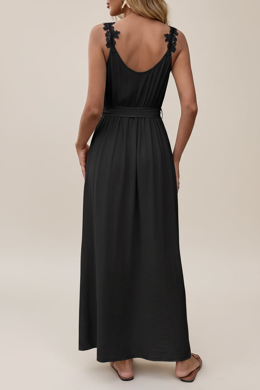 Woman wearing a black dress with lace details standing against a neutral wall.