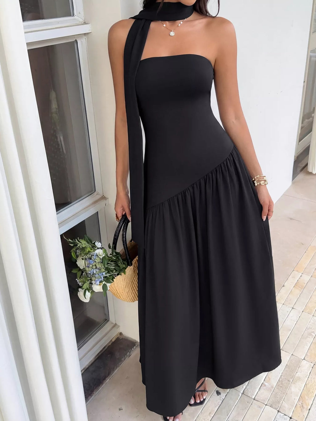 Woman wearing a black halter neck dress holding a woven bag with flowers.