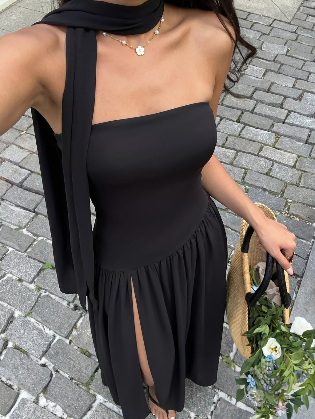 Woman wearing a black one-shoulder dress on a paved street.
