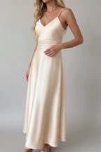 Woman wearing a beige dress standing in front of white curtains.